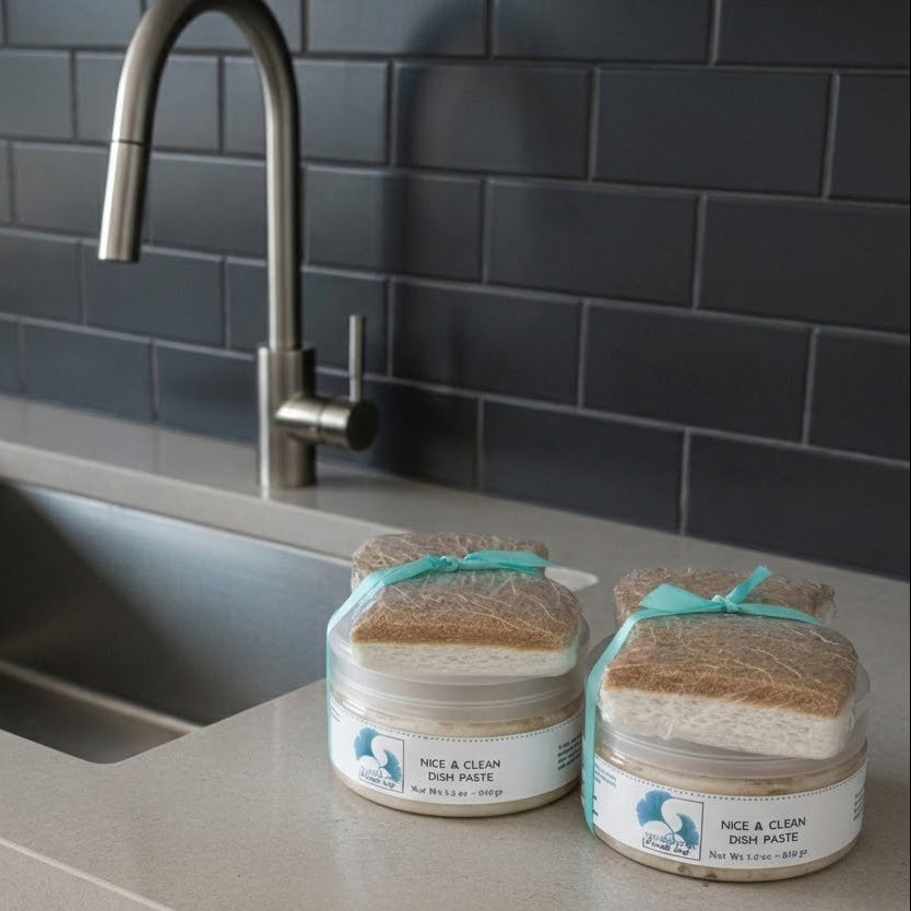 Two jars of Nice & Clean Dish Paste on a kitchen counter with a sink and tiled wall in the background.
